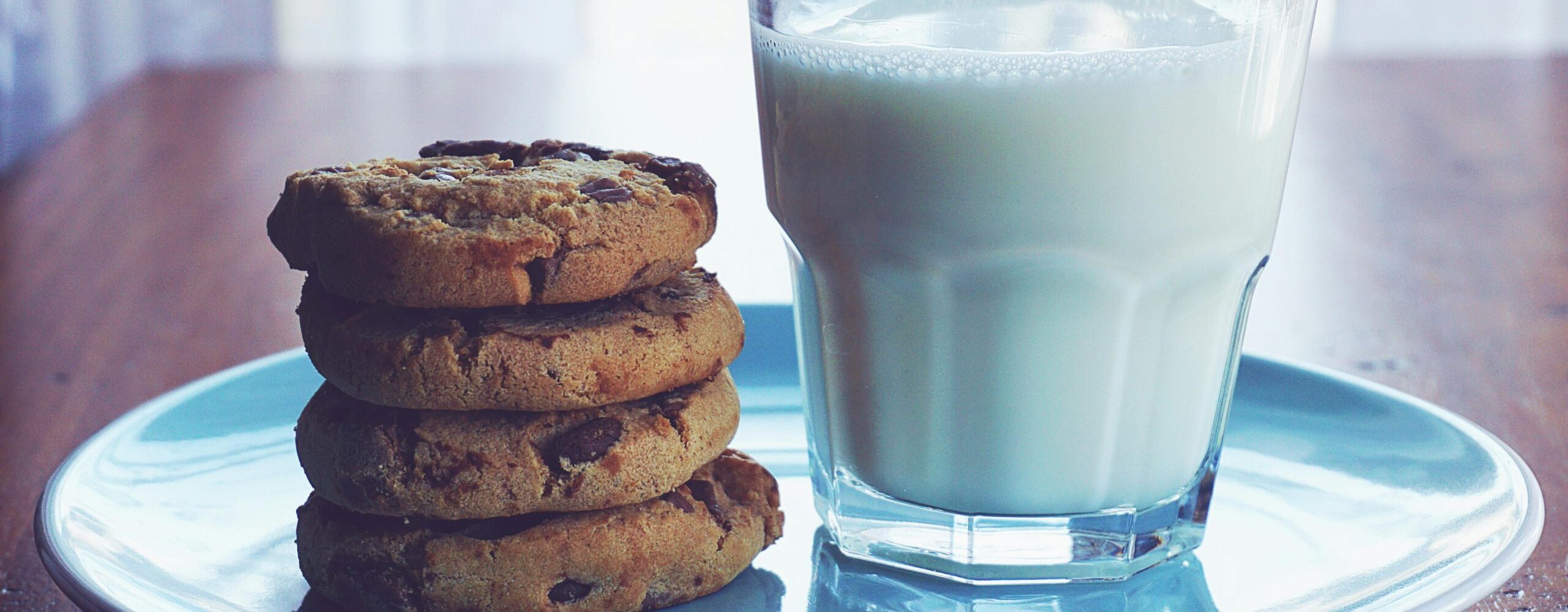 Close-up of chocolate chip cookies stacked beside a glass of milk on a blue plate.