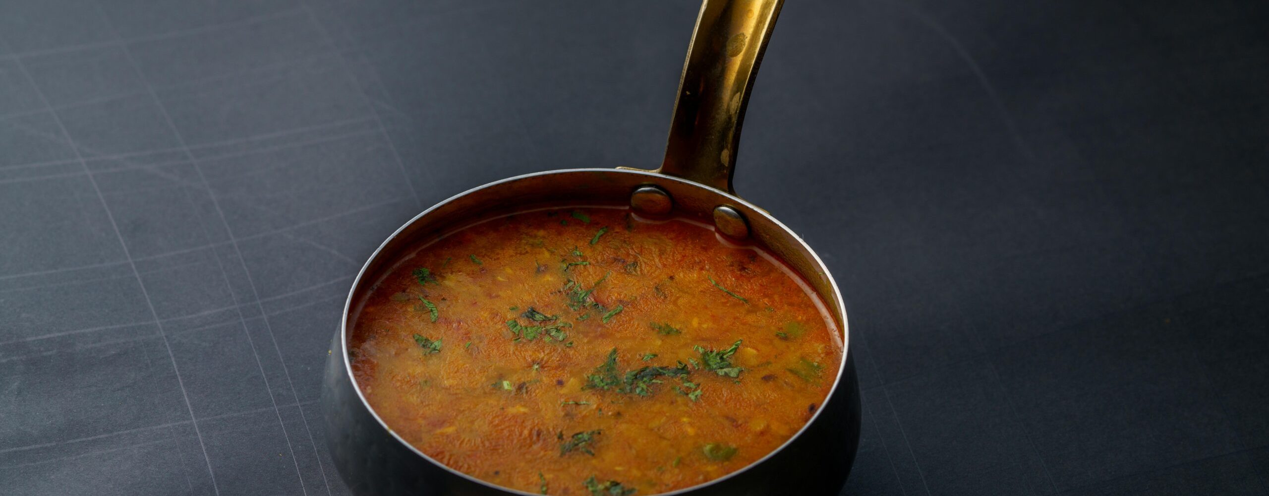 A close-up shot of Indian dal garnished with herbs in a copper pot, offering a taste of traditional cuisine.